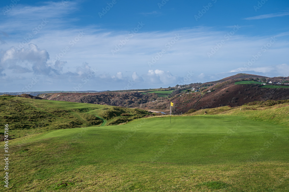 A pristine golf green, with the flag in, on a links course on the Welsh coastline.  The golf course is Pennard Golf Course over looking the Three Cliffs Bay