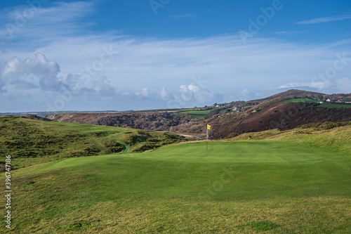 A pristine golf green, with the flag in, on a links course on the Welsh coastline. The golf course is Pennard Golf Course over looking the Three Cliffs Bay