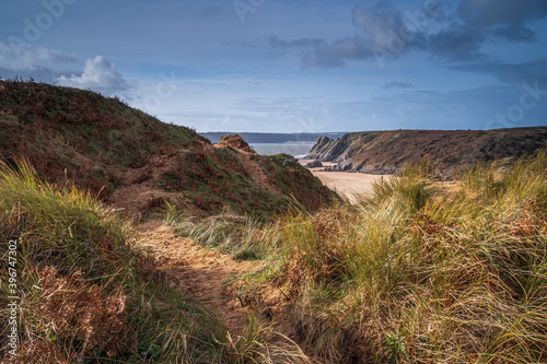 A path through grassy sand dunes, on the Welsh coastal path, overlooking a majestic beach