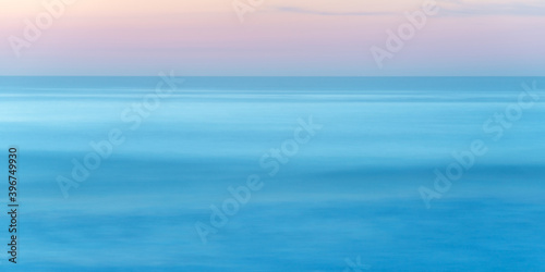 Long exposure of seascape at sunset, blue sea water abstract background, pastel pink sky