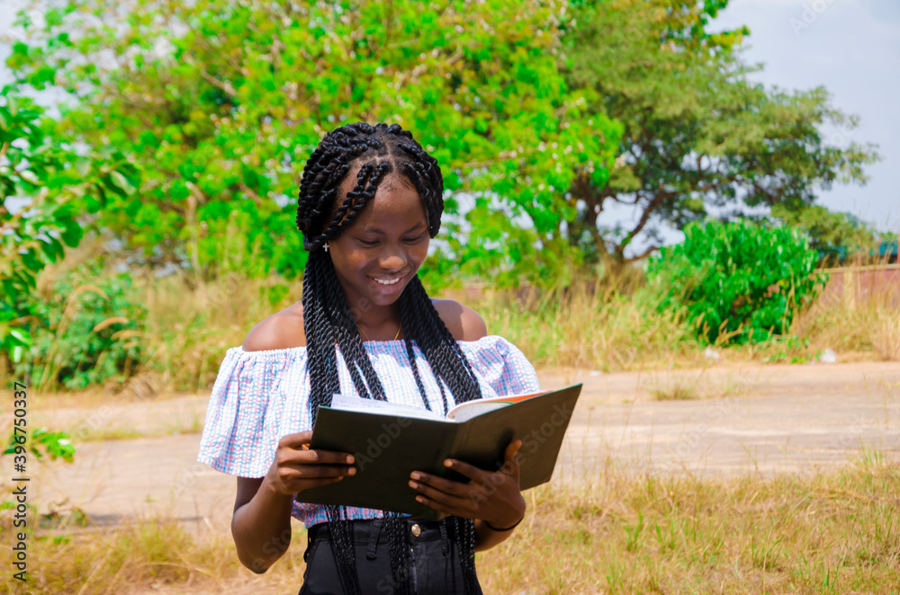 Fototapeta premium a young beautiful african school student feeling excited as she is going through her notebook.