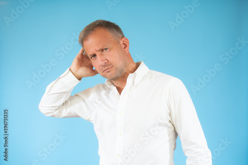Young man in casual shirt thinking over blue background. © Danko