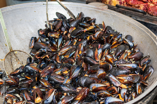 A large number of freshly prepared mussels are in a metal cauldron. Delicious food cooked over an open fire, which is offered at a street food fair, event, festival.