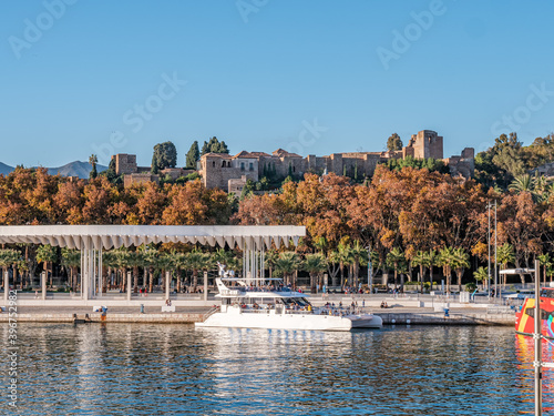 View of the "Muelle Uno" outdoor shopping mall, the marina, main park, Pompidou museum and the port of Malaga on a sunny day.Alcazaba, the arab castle and the cathedral in the background.