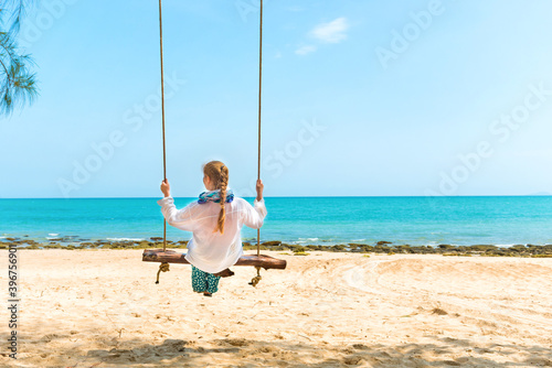 Happy pretty young woman swinging on beach swing at tropical island