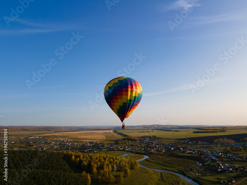 Multicolored hot air balloon flies over the village