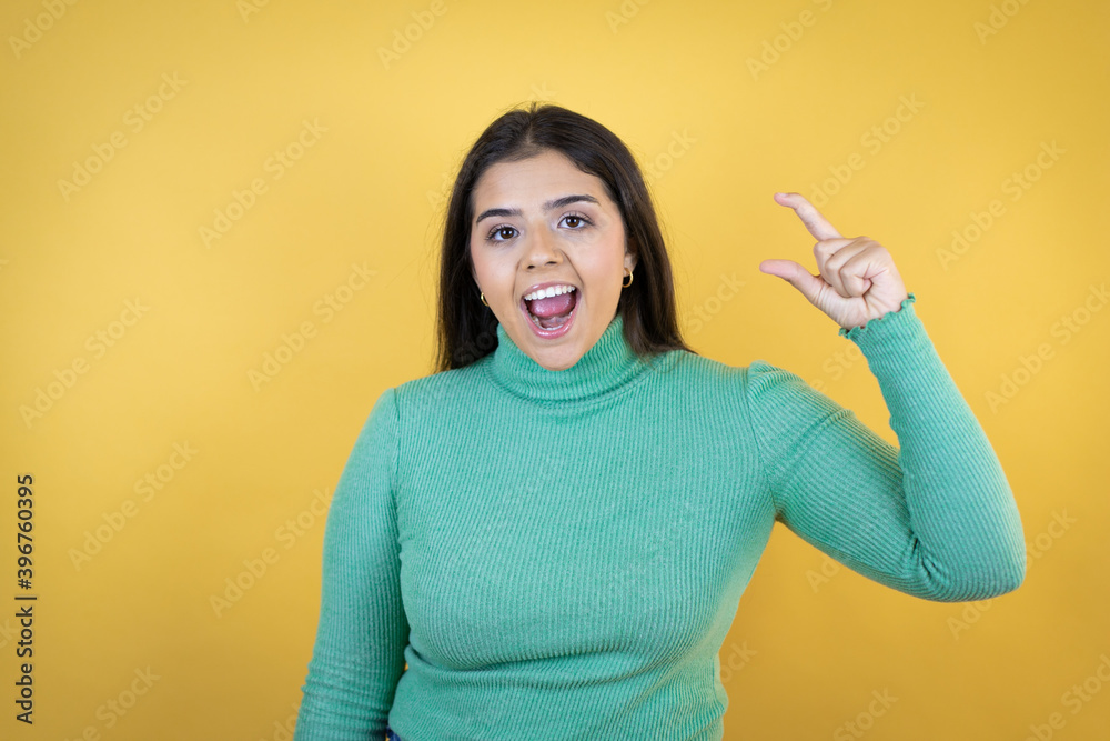 Young caucasian woman over isolated yellow background smiling and confident gesturing with hand doing small size sign with fingers . Measure concept. Young caucasian woman over isolated yellow background smiling and confident gesturing with hand doing small size sign with fingers . Measure concept.