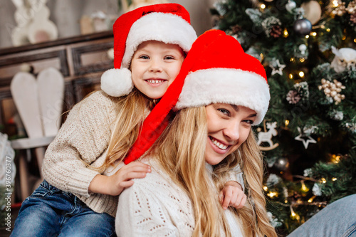 Portrait of happy mother in santa claus and daughter near christmas tree at home. Merry Christmas