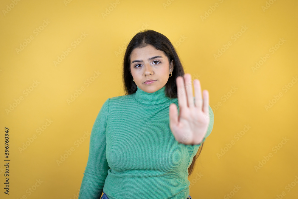 Young caucasian woman over isolated yellow background serious and doing stop sing with palm of the hand. Young caucasian woman over isolated yellow background serious and doing stop sing with palm of the hand.