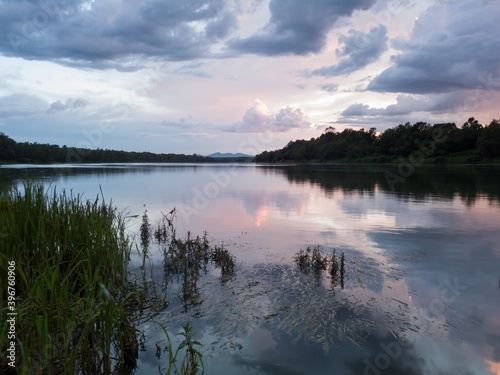 Принти на полотні Landscape with river, clouds, water grass and mountain in distance at sunset