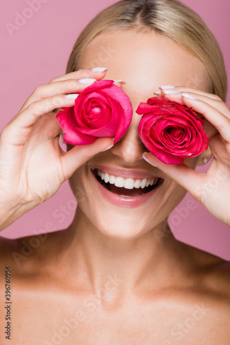 smiling beautiful blonde woman with rose flowers on eyes isolated on pink