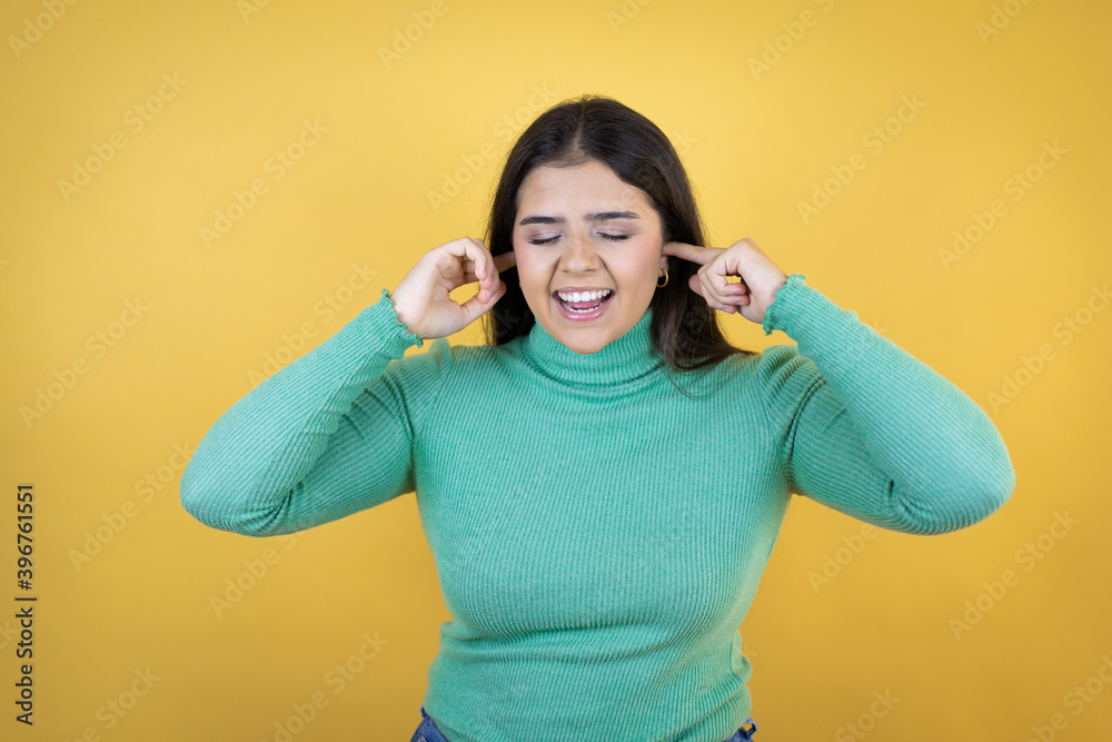 Young caucasian woman over isolated yellow background covering ears with fingers with annoyed expression for the noise of loud music. Deaf concept. Young caucasian woman over isolated yellow background covering ears with fingers with annoyed expression for the noise of loud music. Deaf concept.