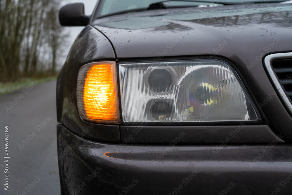 Close-up of the right headlight of a gray car with the emergency light on.