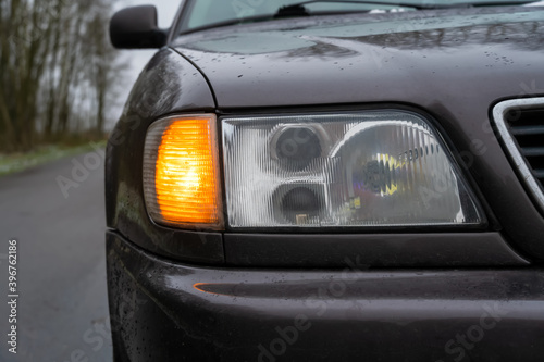 Close-up of the right headlight of a gray car with the emergency light on.