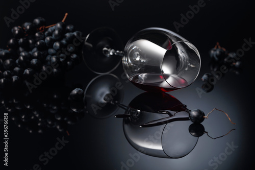 Blue grapes and wine glass with red wine on a black reflective background.