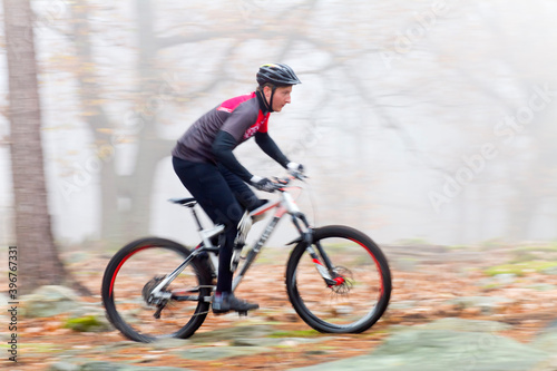 Man cycling with mountain bike in a forest with fog in the background