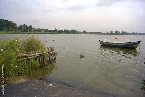 Obraz na płótnie A fishing boat with ducks on a lake on a cloudy day w salonie