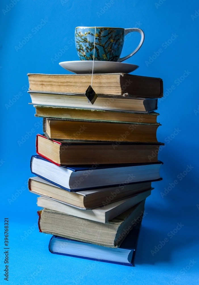 a stack of books on which stands a tea mug with a tea bag, blue background a stack of books on which stands a tea mug with a tea bag, blue background