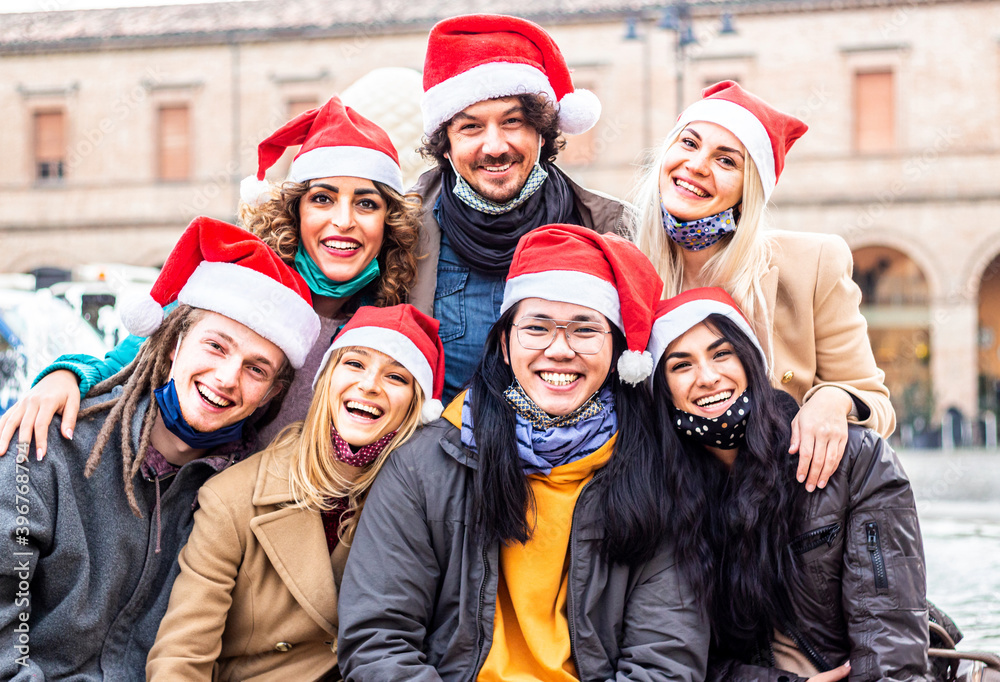 Happy people with Santa Claus hats celebrating Christmas - New normal lifestyle concept with young friends wearing face mask enjoying xmas eve.