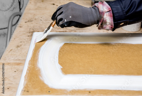 Repainting kitchen cabinet doors with white chalk paint indoors at home. Giving old kitchen new look concept. Hand holding a paint brush tool with paint against old cupboard door. photo