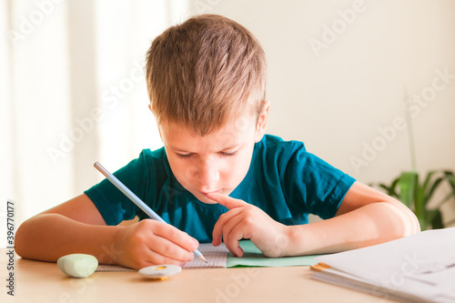7 years old child boy doing lessons sitting at desk in his room.