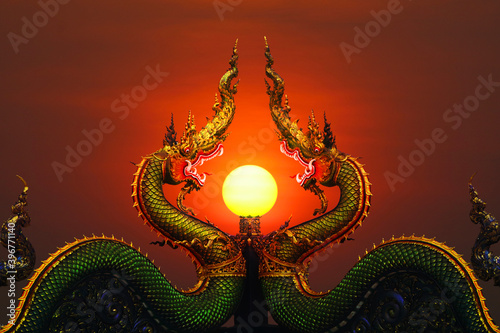 Two Naga status and pole in middle and sunset red sky on top of pole clear evening cloud