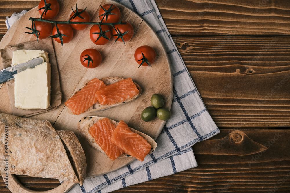 Two sandwiches with smoked salmon and other food on old board on rustic wooden background. Top view Two sandwiches with smoked salmon and other food on old board on rustic wooden background. Top view