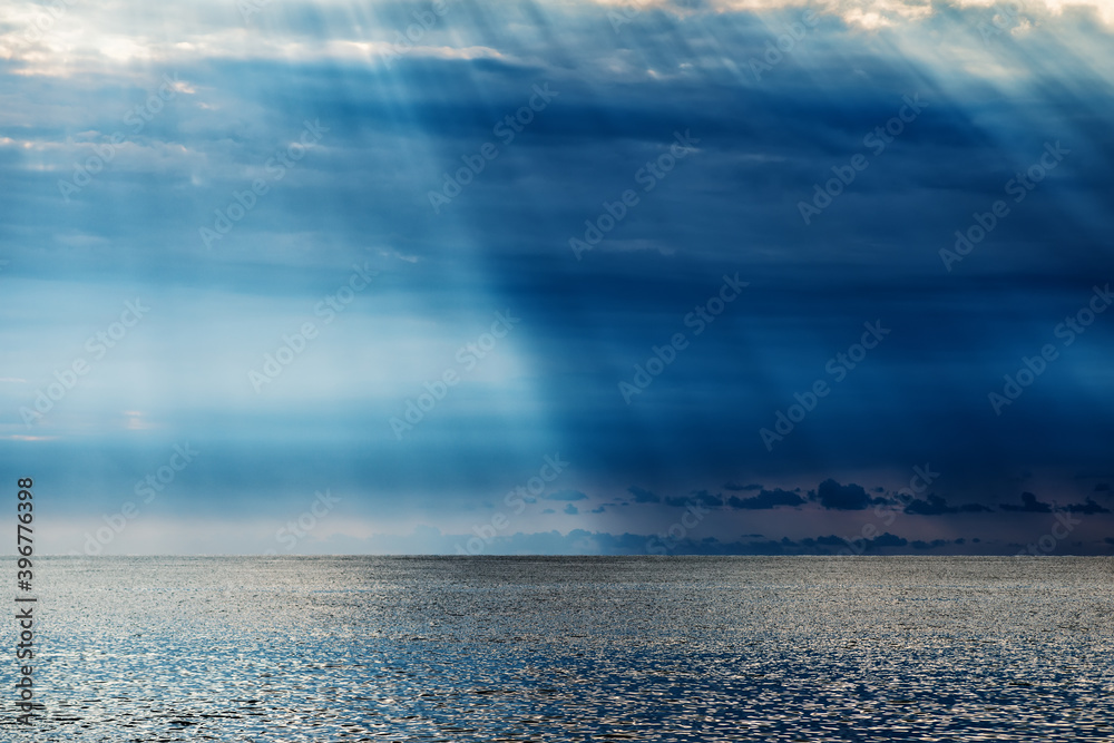 A sunbeam dividing the frame in half through dark clouds over the sea with reflection