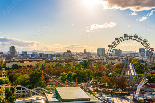 City view of Vienna, Austria, from above at Prater amusement park. Iconic fairy wheel and other amusement rides in the background with the sun peeking out of the clouds.