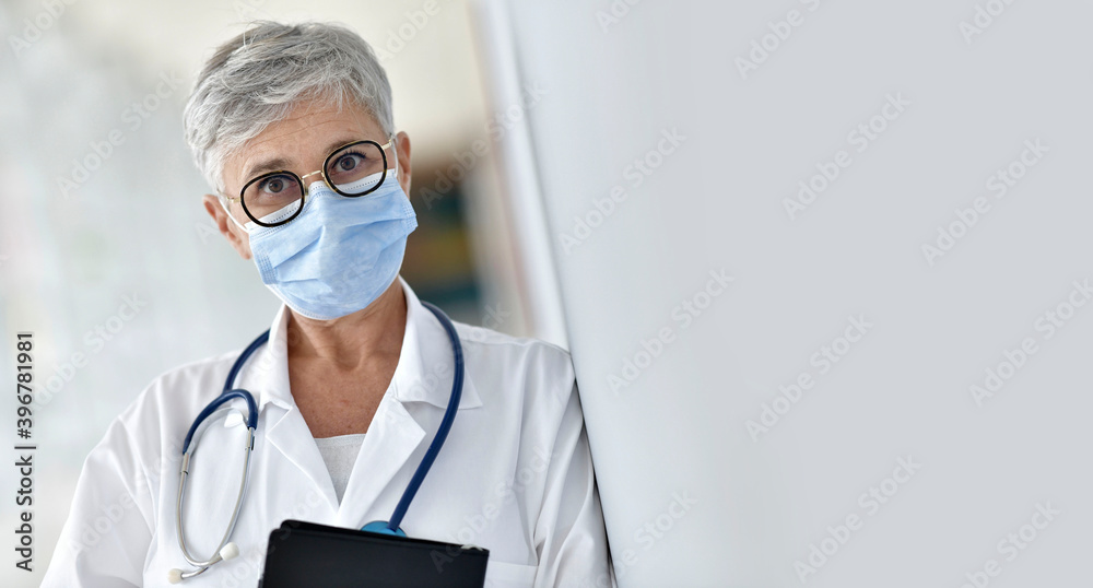 Portrait of mature woman doctor standing in hospital hallway with face mask on
