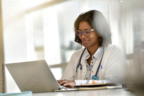 Woman doctor working in office with laptop computer; wearing face mask