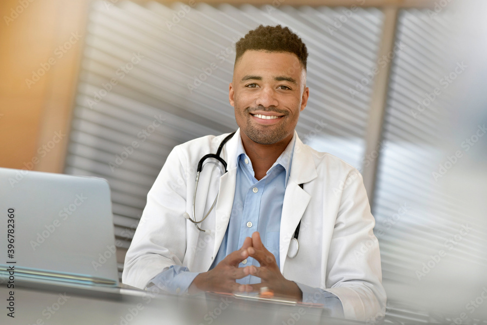 Portrait of smiling doctor sitting at desk, looking at camera Portrait of smiling doctor sitting at desk, looking at camera