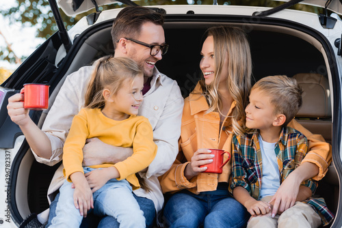 Smiling parents with cups hugging kids in trunk of car