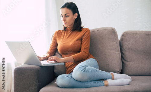 Young confident beautiful woman working with her laptop while sitting on the couch at home