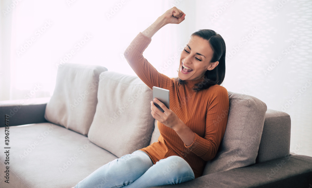 Fototapeta premium Happy excited beautiful woman with smart phone on the couch