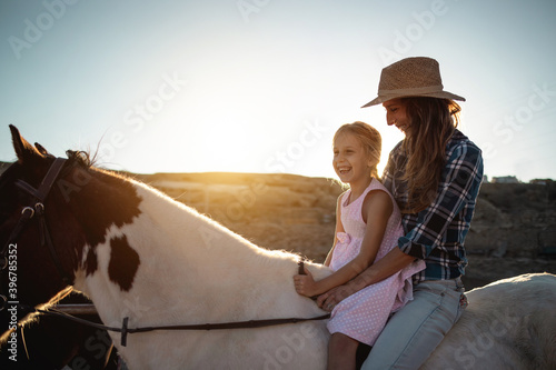 Happy mother and daughter riding a horse at sunset - Family and love concept - Focus on kid face