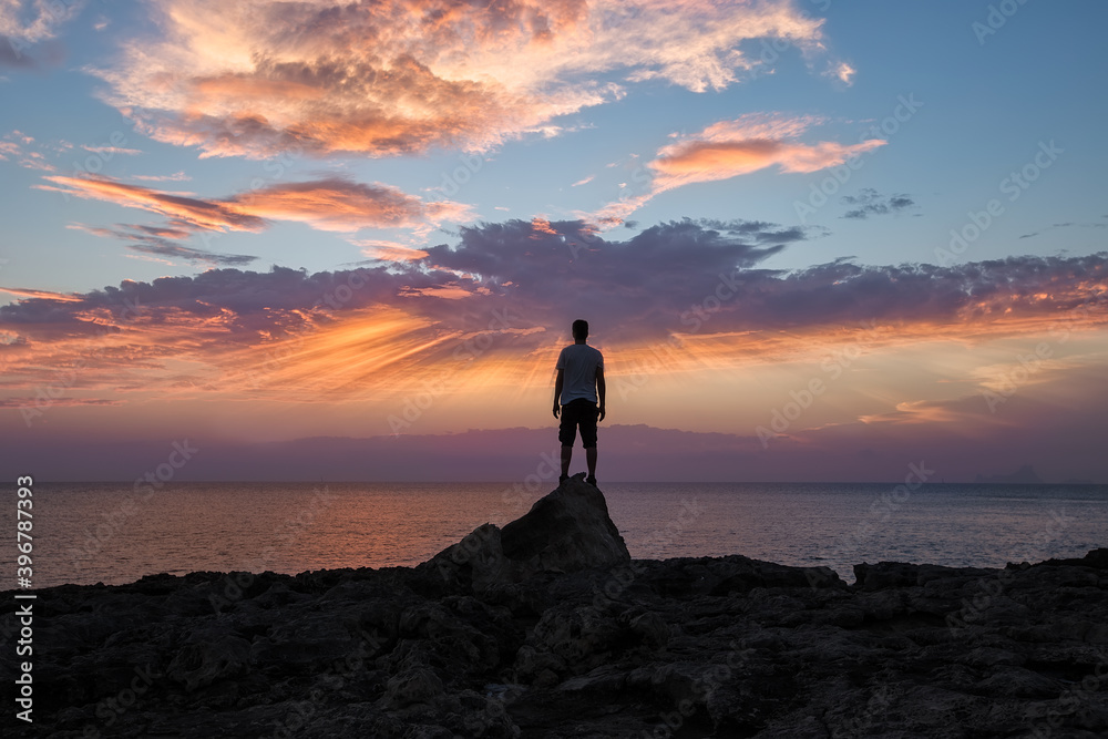 man with his back on a rock, watching the sunset over the sea