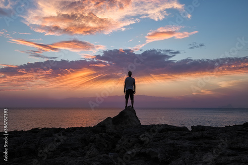 man with his back on a rock  watching the sunset over the sea
