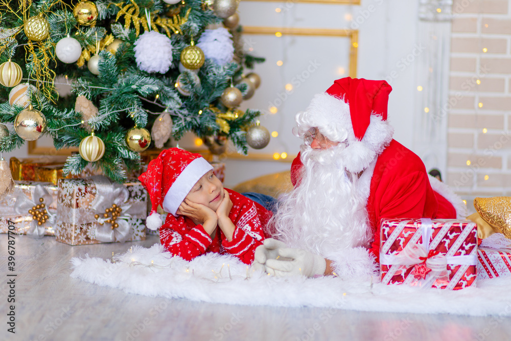 Fototapeta premium child and Santa Claus near the Christmas tree, boy looks at Santa Claus