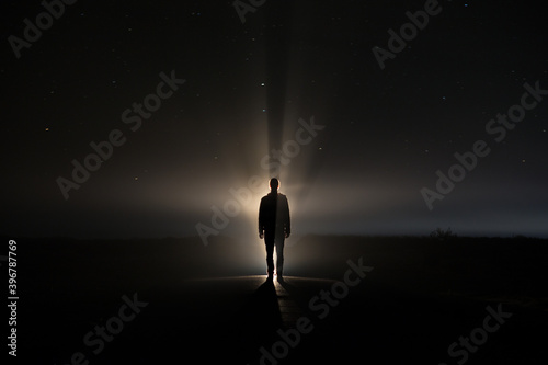 Fotobehang backlighting of a man in the dark of a foggy night and a light behind the model