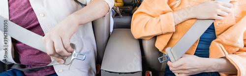 Cropped view of parents holding safety belts near child on blurred background in car, banner