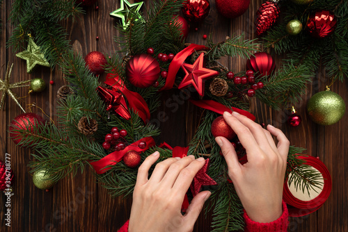Florist hands making Christmas wreath on wooden brown background. Top view. New Year or Christmas celebration concept