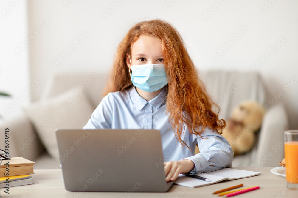 Schoolgirl in medical mask studying at home with digital laptop Schoolgirl in medical mask studying at home with digital laptop