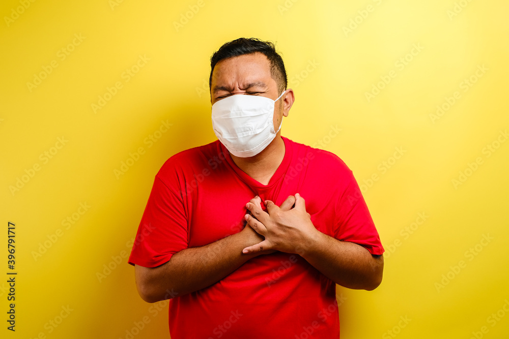 Asian guy wearing mask feeling pain in his chest, gesture holding left chest Asian guy wearing mask feeling pain in his chest, gesture holding left chest