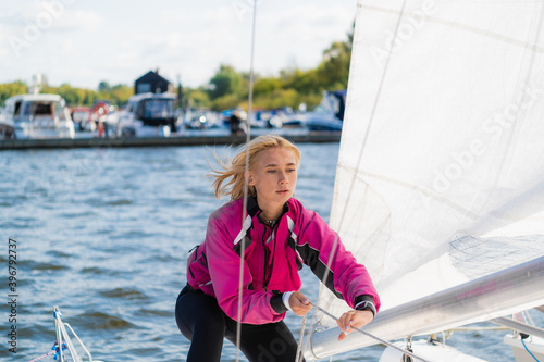 Cute blondes on the pier prepare a sailing yacht for a regatta, pull the sail on the mast with ropes.