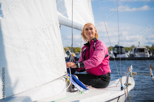 A young female sailing athlete sets a genaker sail on her white sports yacht to go to a regatta