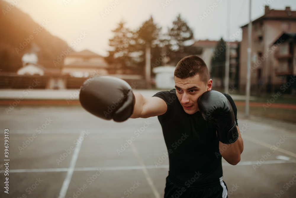 Photo of young masculine man in boxing gloves at playground outdoors. Portrait of young man in boxing gloves