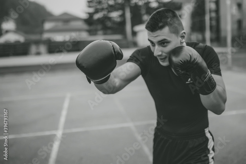 Photo of young masculine man in boxing gloves at playground outdoors. Portrait of young man in boxing gloves