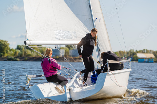 A fast, sporty, single-masted yacht with three athletes on board sails with a fair wind on a beautiful river