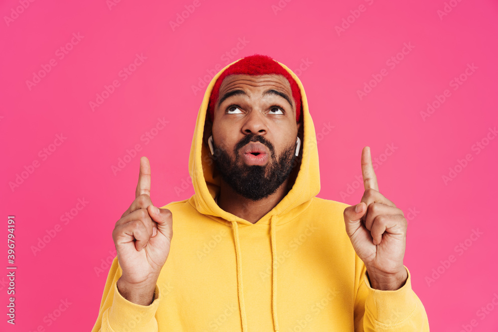 Surprised african american guy in earphones pointing fingers upward Surprised african american guy in earphones pointing fingers upward